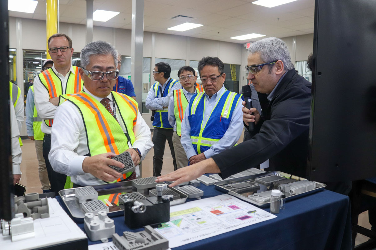 John Baciak (right) points to recent 3D printing projects during a tour of NAPIC’s ADM center with DENSO Chairman of the Board Koji Arima (left) and Shinichi Nakamizo in April 2024.