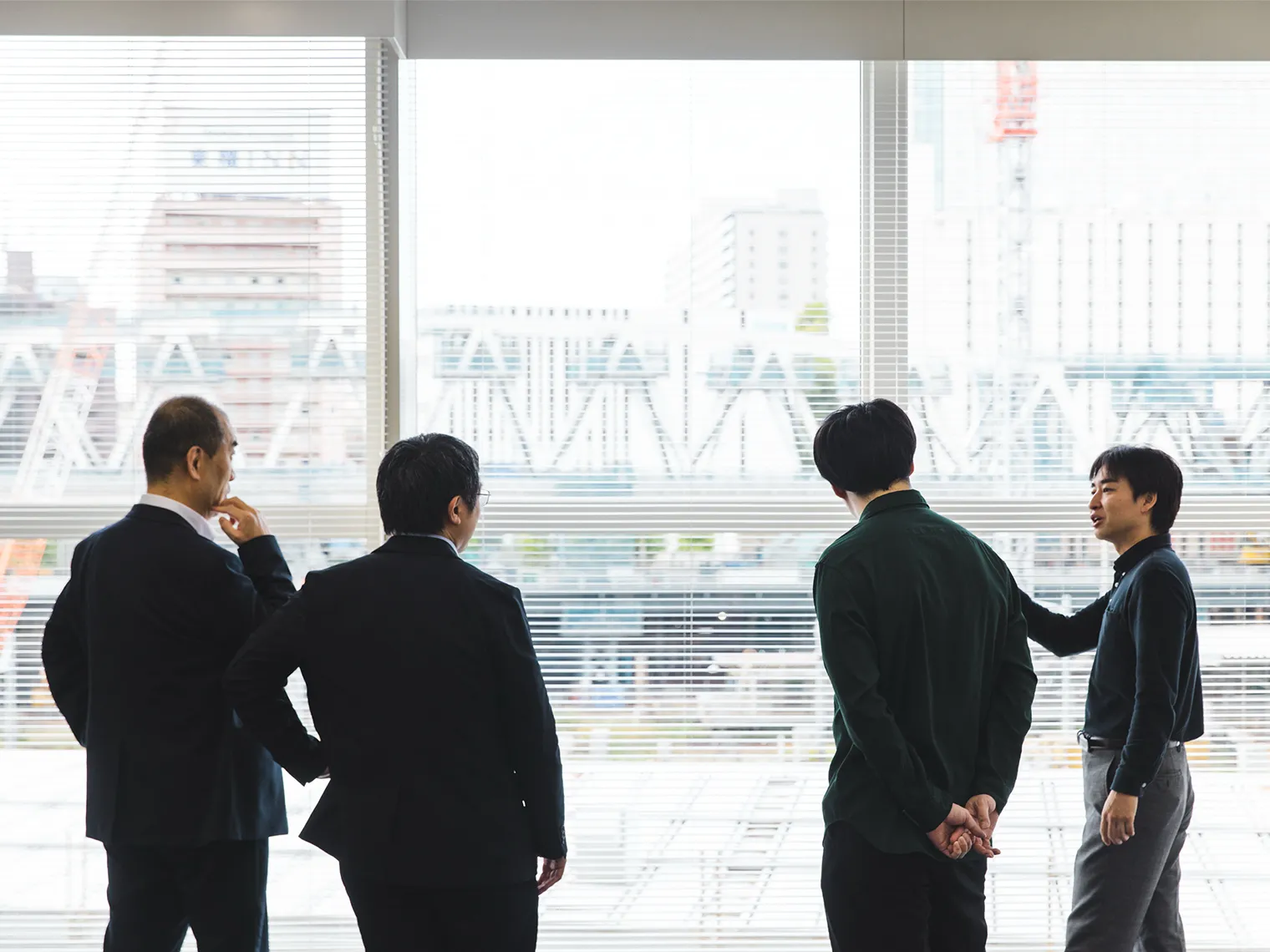 窓辺で立ち話をする岩城、田辺、西、平井の4名