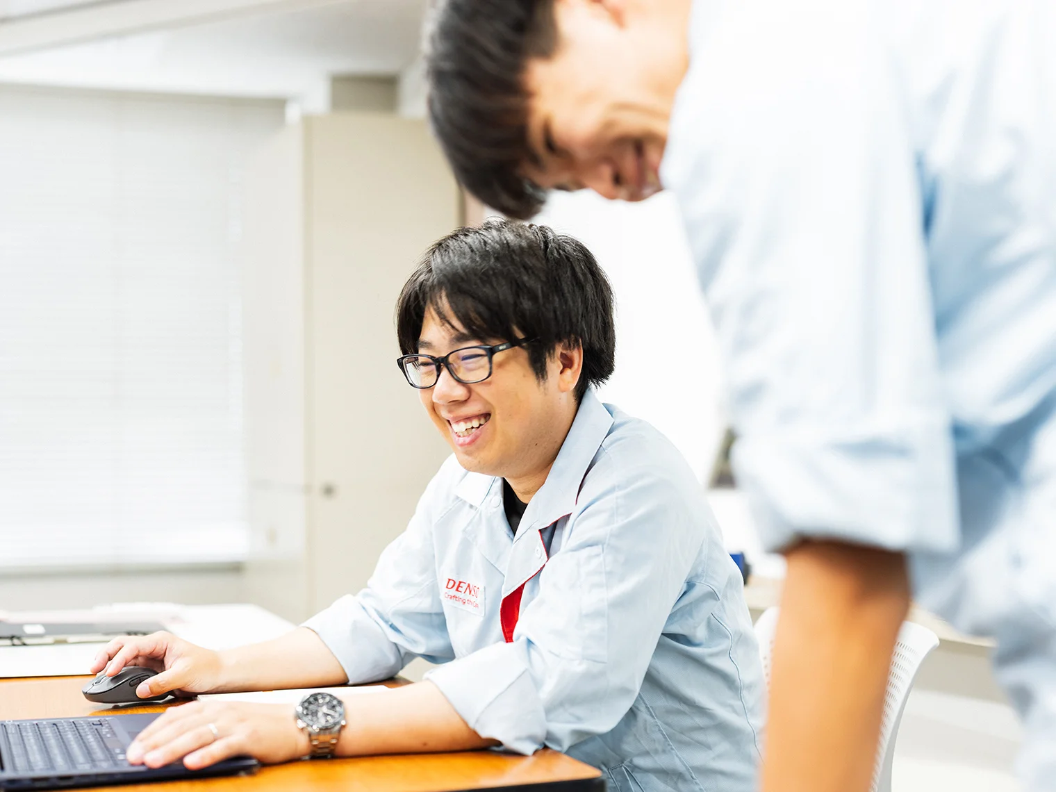 同僚とPCを見ながら笑顔を交わす沓名 佑太