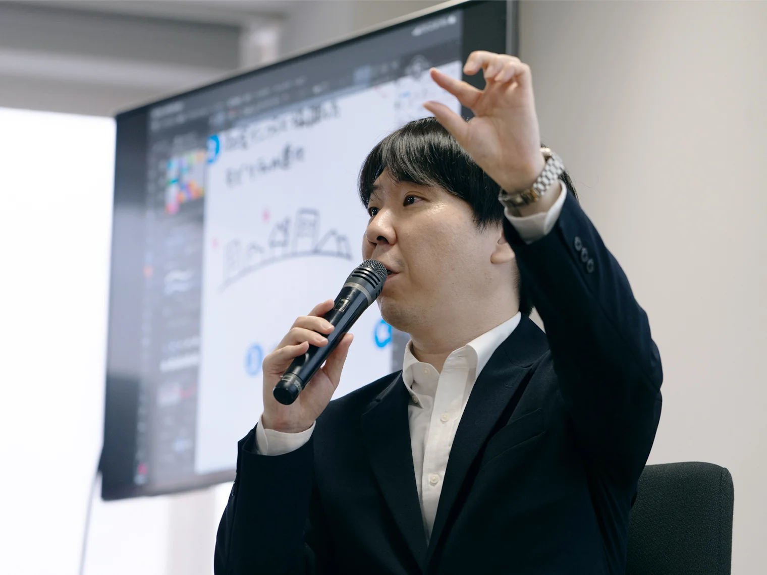 マイクを持ち、身振り手振りで話す本間准教授