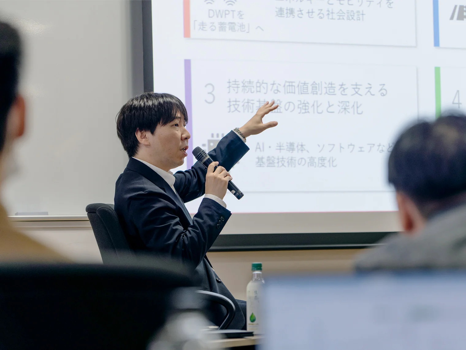 スクリーンの「持続的な価値創造を支える技術基盤」を指し示しながら話す本間准教授