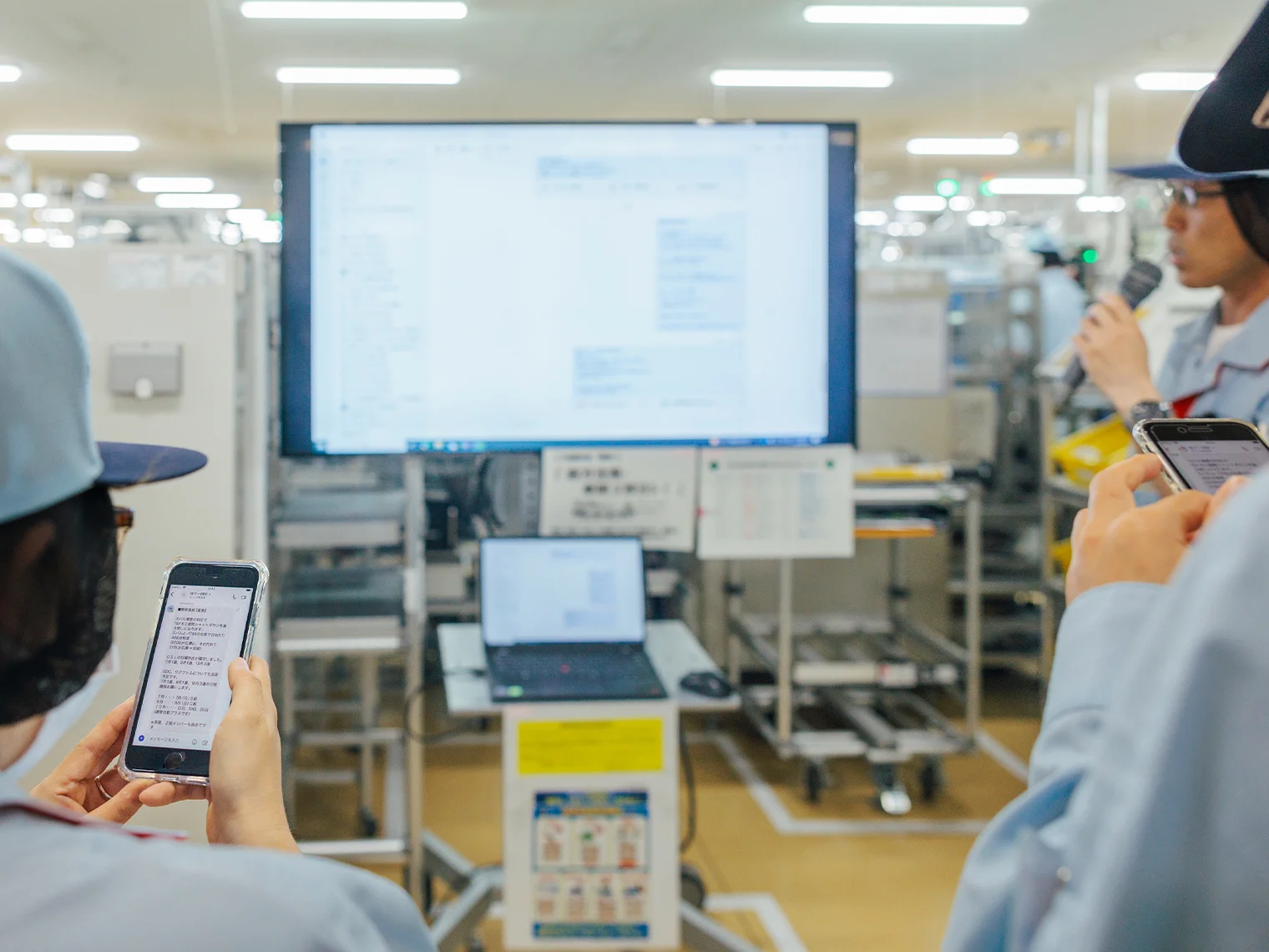 現場にて大型モニターに映し出された画面を各自デジタルデバイスで確認する様子