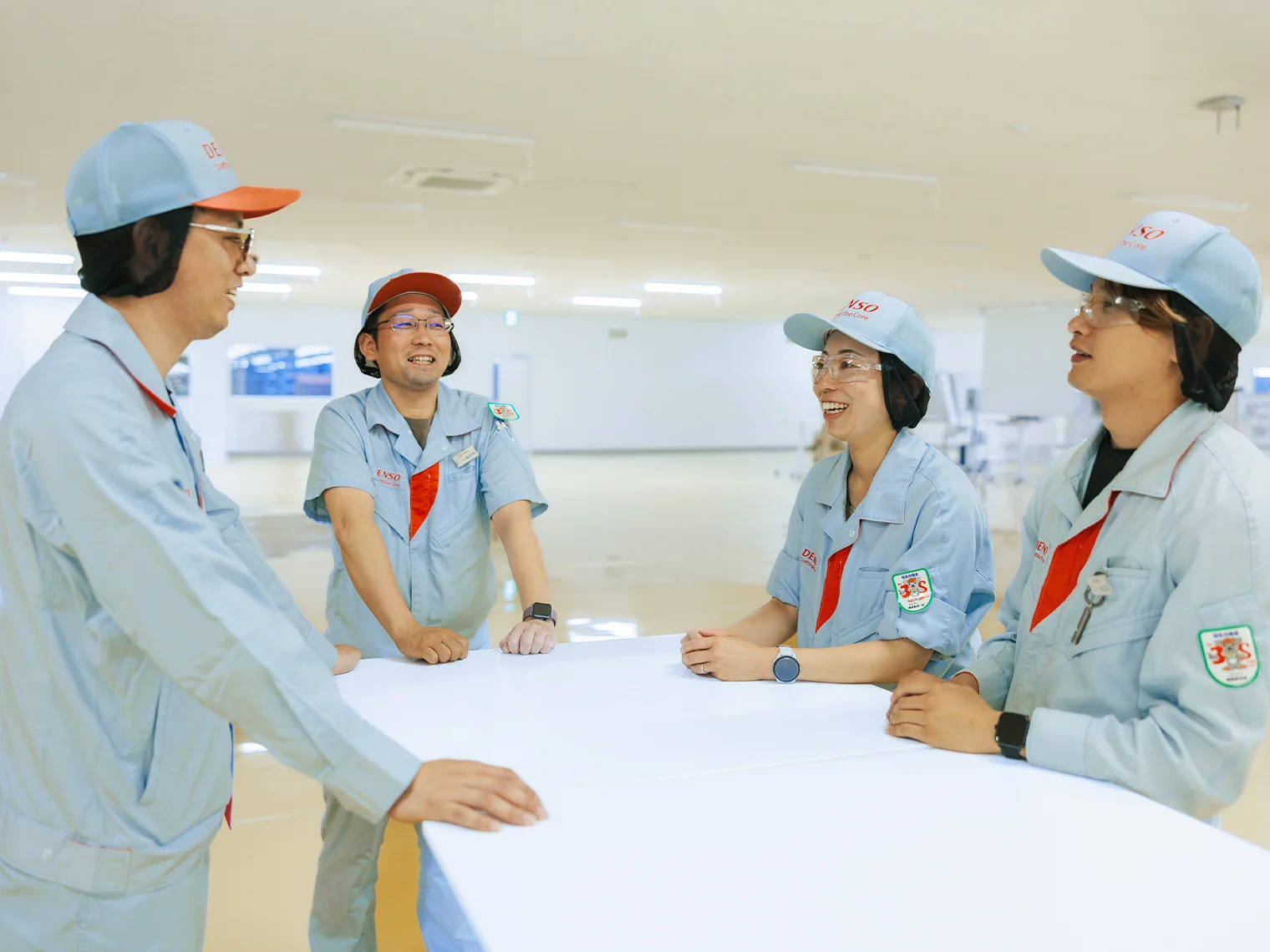 作業着を着た4人の社員がテーブルを囲んで笑顔で会話する様子