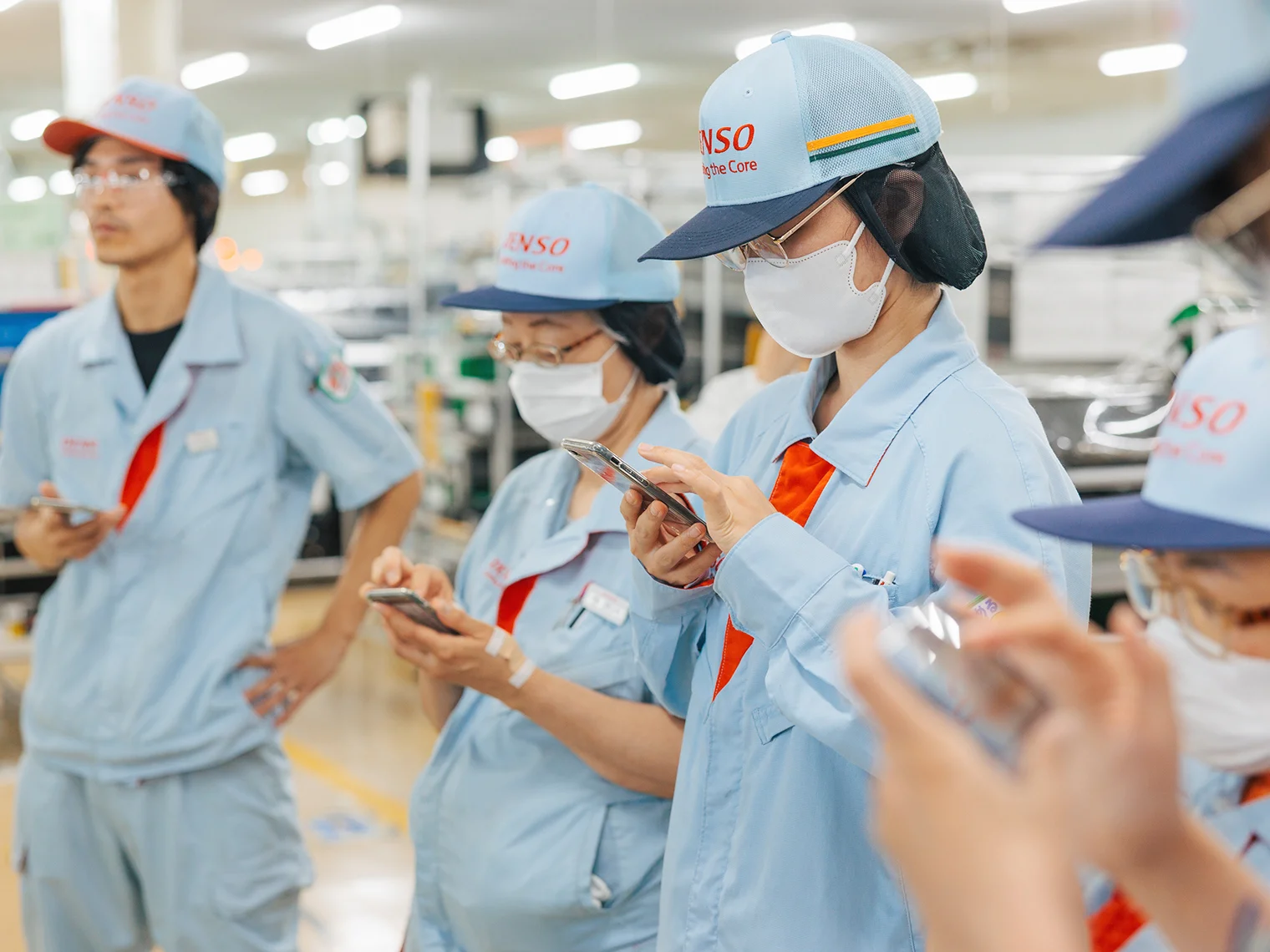 工場内で作業着を着た複数の社員がスマートフォンを操作している様子