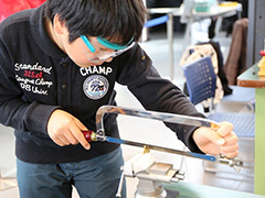 写真は、弓のこを使い切断作業をしている様子