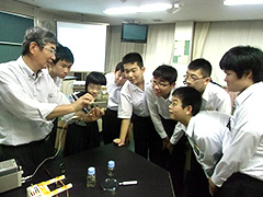 写真は、磁力線を観察する器具を覗き込む生徒たちの様子