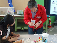 写真は、指導員がコツを伝えながら、参加者の工作をサポートしている様子