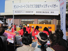 写真は、赤いジャンパーを着た社員ボランティアが商品を並べて準備している様子