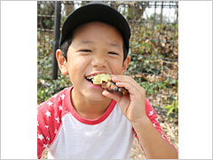 写真は、参加した男の子が笑顔で美味しそうに焼き芋を食べている様子