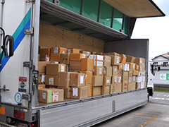 写真は、トラックの幌が上がり、衣料の詰められた沢山のダンボールが荷台を埋め尽くしている様子