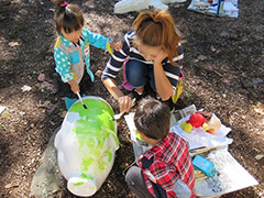 写真は、親子3人で子ブタのオブジェにペンキを塗っている様子