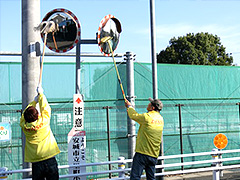 写真は、きいろジャンパーを着た参加者2名がモップを持ち、腕を伸ばしてカーブミラーを拭いている様子