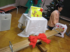 写真は、寄贈した木製の室内用シーソーに赤い大きなリボンがかけられている様子
