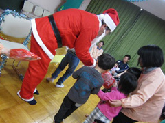 写真は、サンタに扮した社員から園児一人一人へ赤い袋のお菓子をプレゼントしている様子
