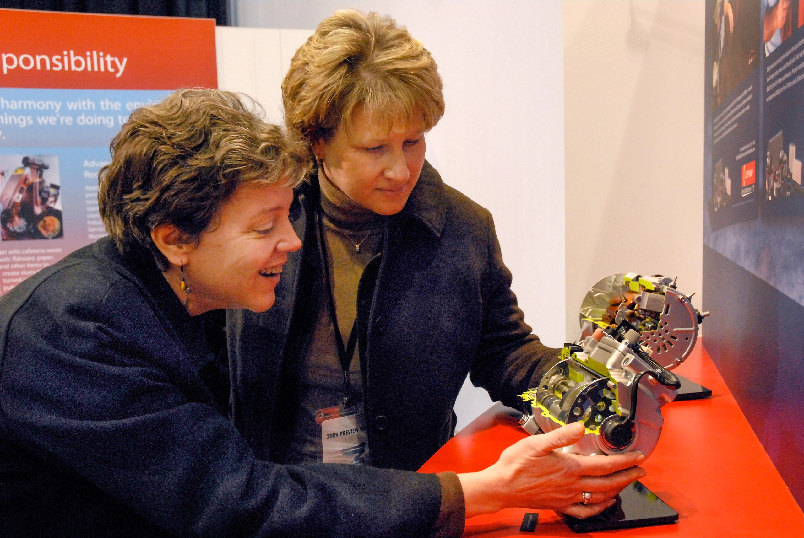 Two Women inspect a part on display