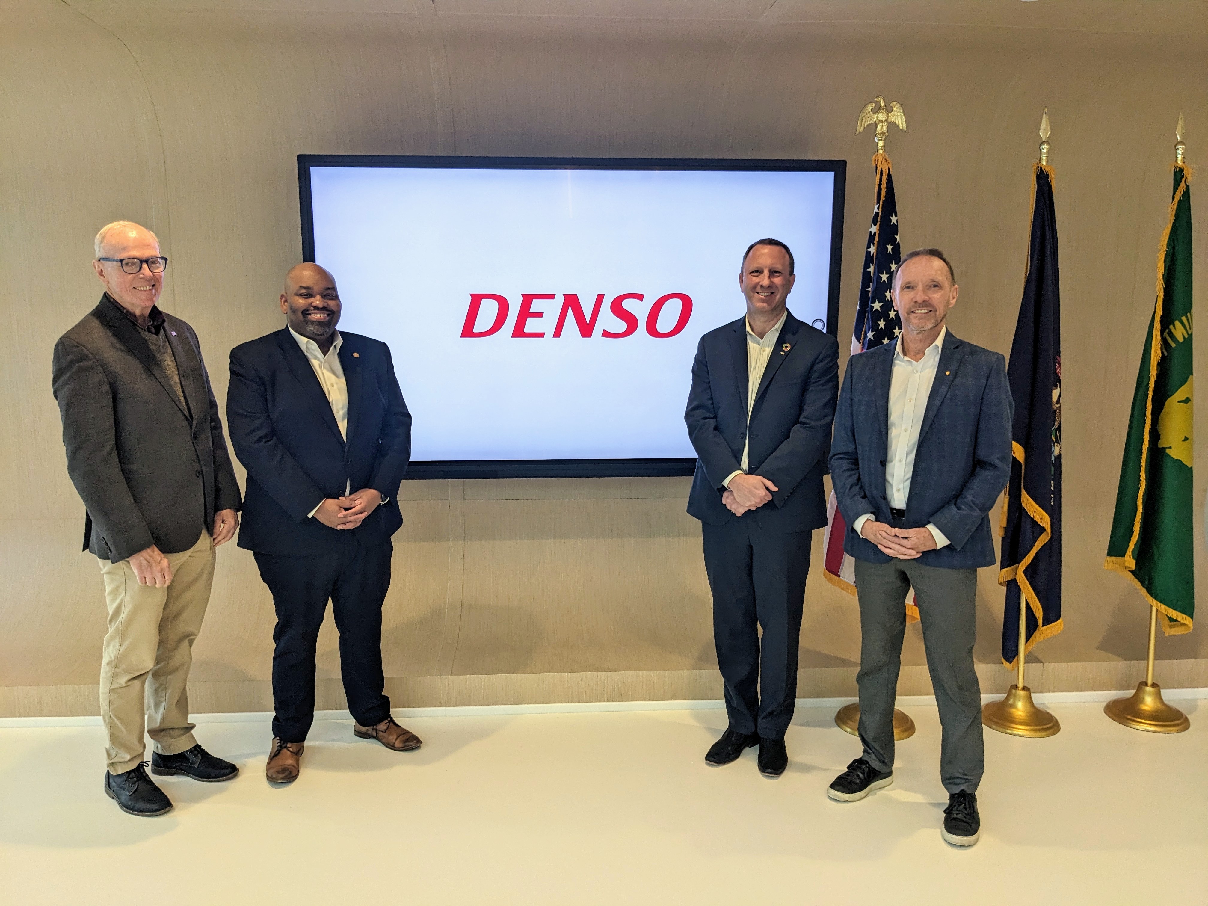 People standing in front of denso logo